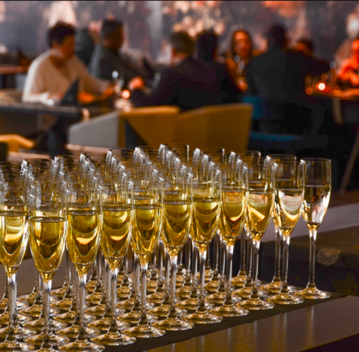 image with many wine glasses full of white wine in the foreground and seated people in the background.