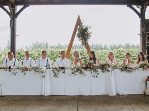 Image of wedding party seated at head table outside in the vineyard.