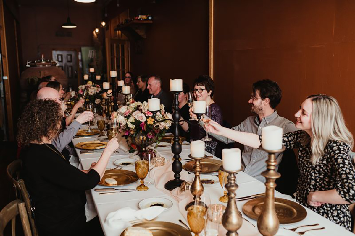 Image of Long table with classy table settings seated with many people having dinner and toasting wine.